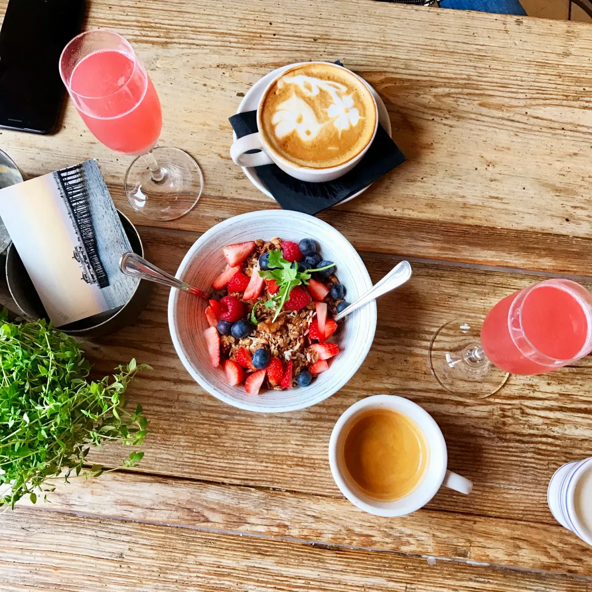 A Cookie Beacon brunch spread — a berry granola bowl, latte art, espresso and pink mimosas on a wooden table