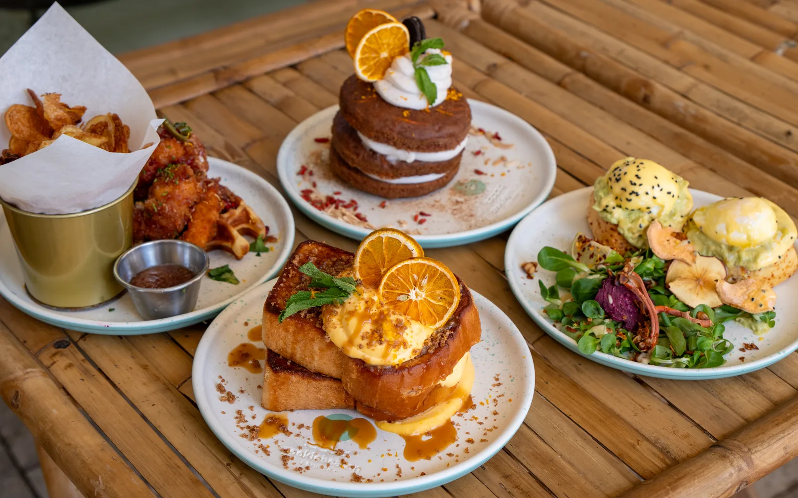 Crème Brûlée French Toast, Carrot-Cake Pancakes, Chicken & Waffles Stack and Eggs Benedict on Cheddar-Scones on a bamboo table at Cookie Beacon