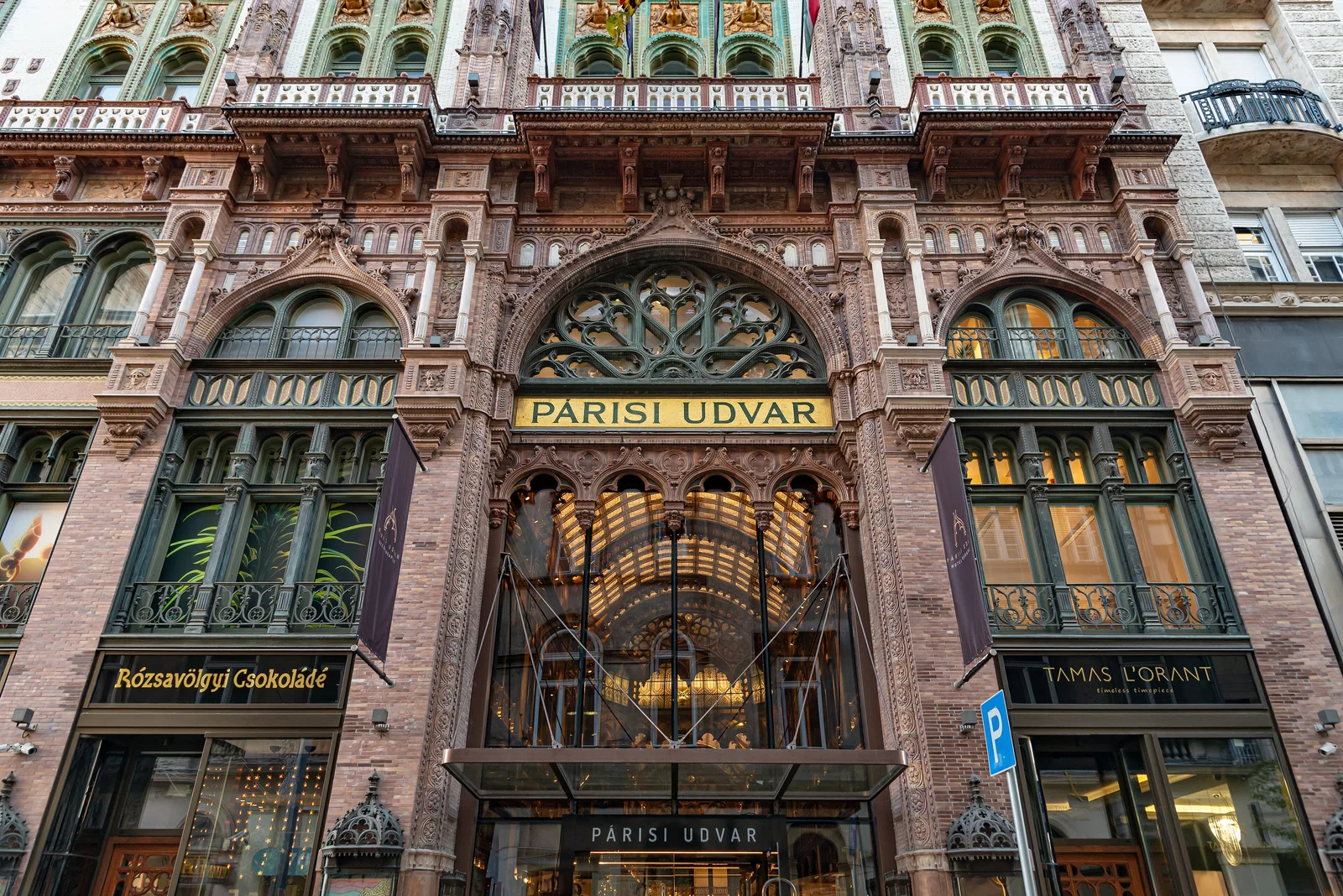 The portal of the Párisi udvar on Ferenciek tere, Budapest: a pointed arch with gold "PÁRISI UDVAR" lettering above a glass and iron entrance, between two shop windows