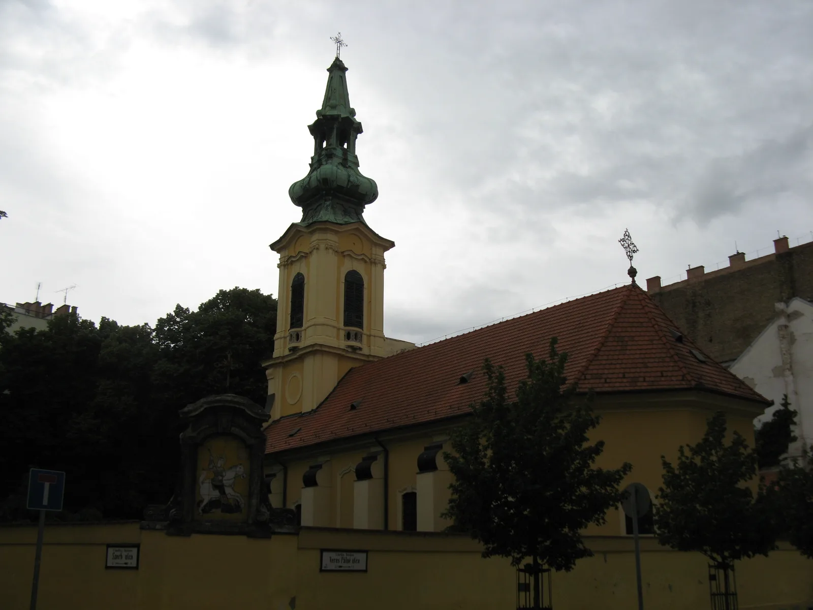 The Serbian Orthodox Church of St George in Budapest: a yellow Baroque church with a green-topped bell tower behind a garden wall, on Szerb utca