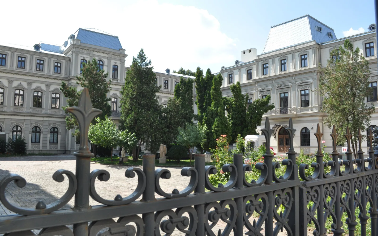The U-shaped Romanit Palace, home of the Museum of Art Collections on Calea Victoriei in Bucharest, seen through its wrought-iron fence with stone sculptures in the courtyard