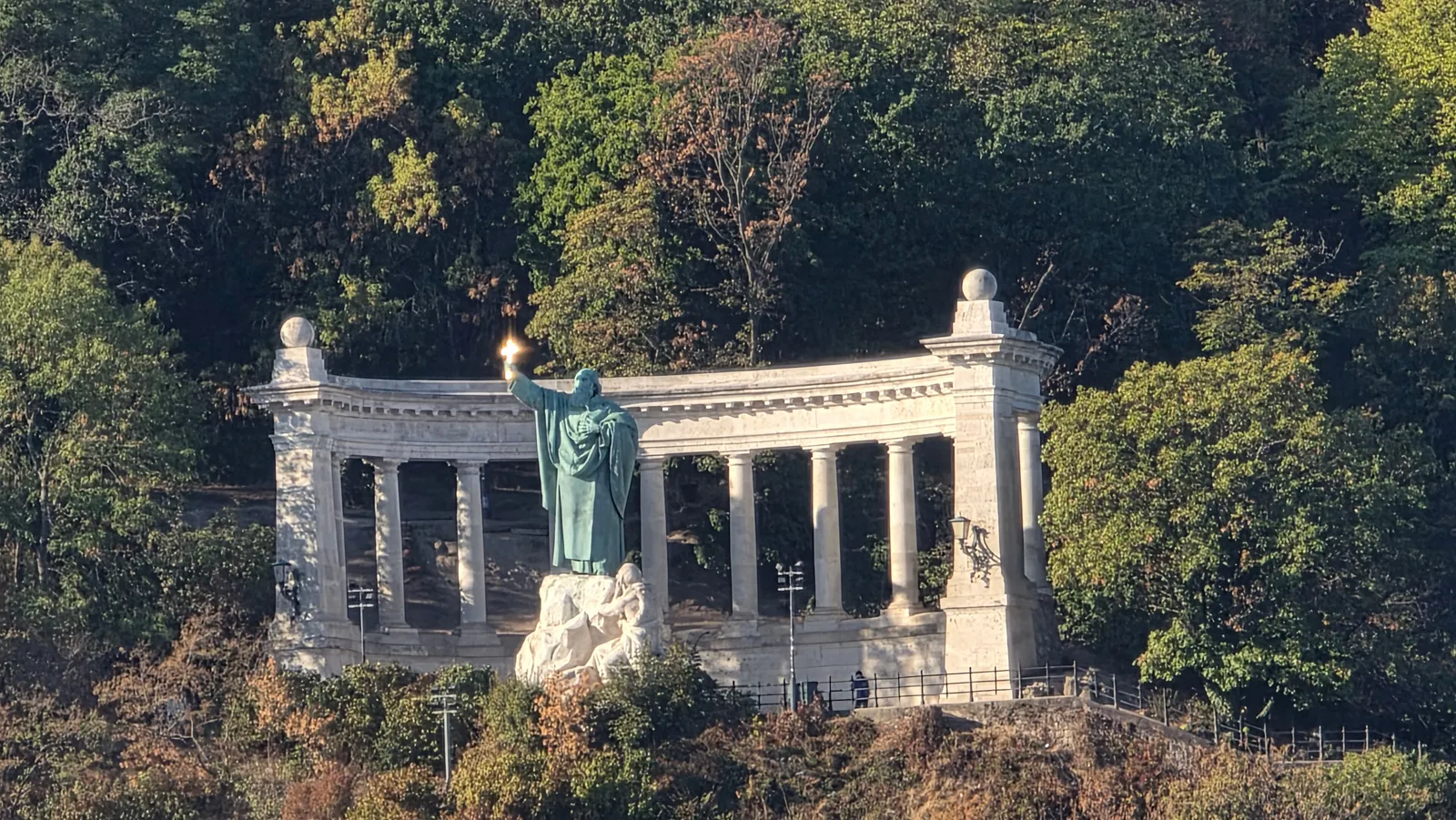 The St Gellért monument on Gellért Hill in Budapest: a bronze bishop raising a cross in front of a white semicircular colonnade, with trees around it