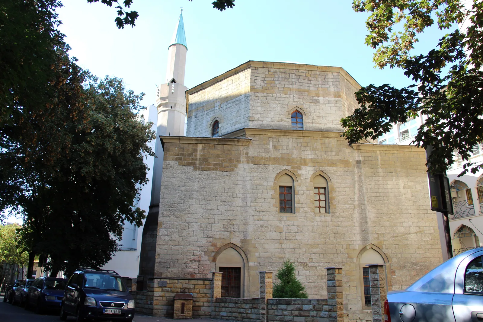 The stone Bajrakli Mosque in Dorćol, Belgrade, with arched windows and a slim white minaret rising behind it, framed by trees on Gospodar Jevremova street