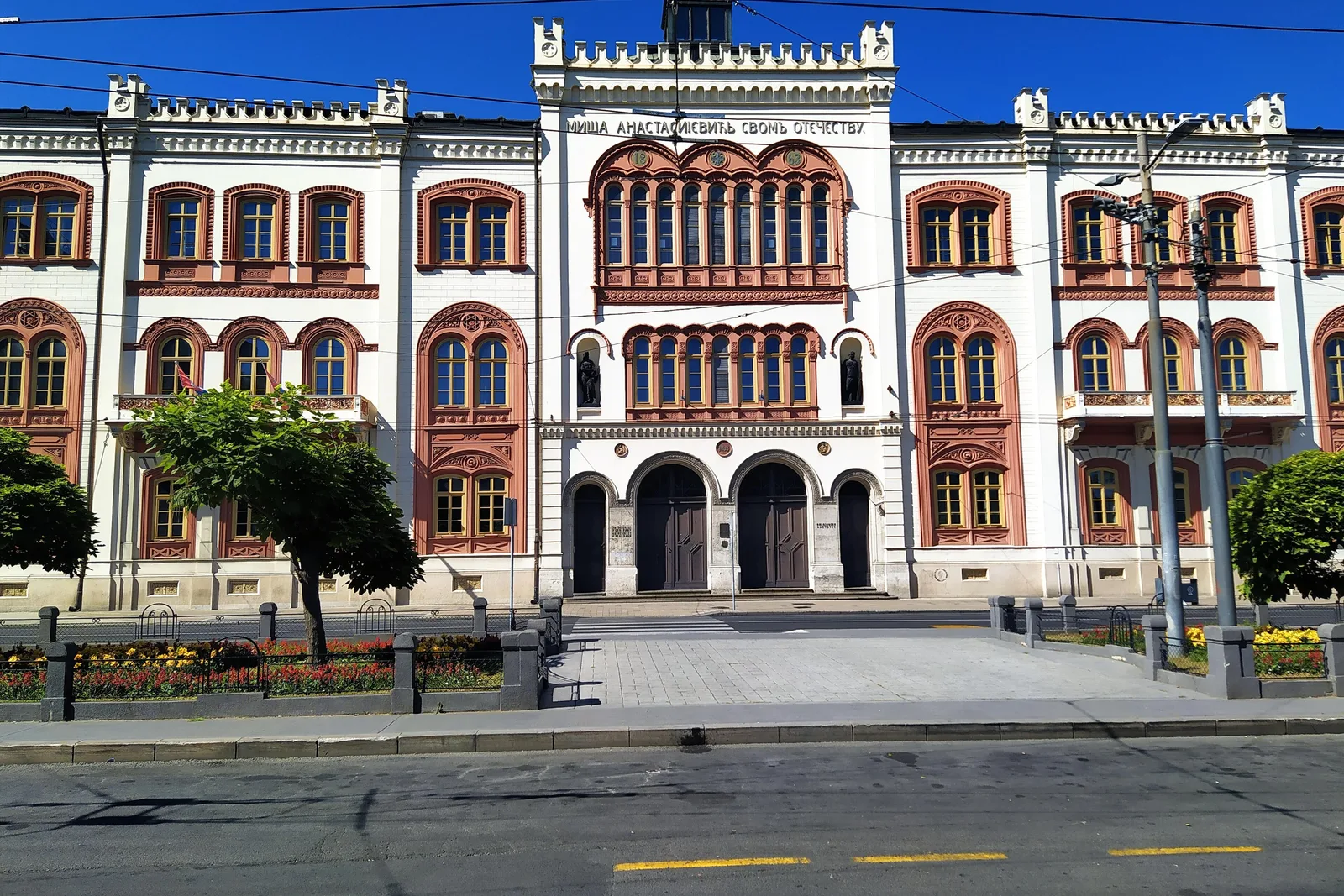 The red-and-cream façade of Captain Miša's Mansion on Studentski trg in Belgrade, with a central bay of arched windows under a crenellated roofline, seen across the street on a sunny day