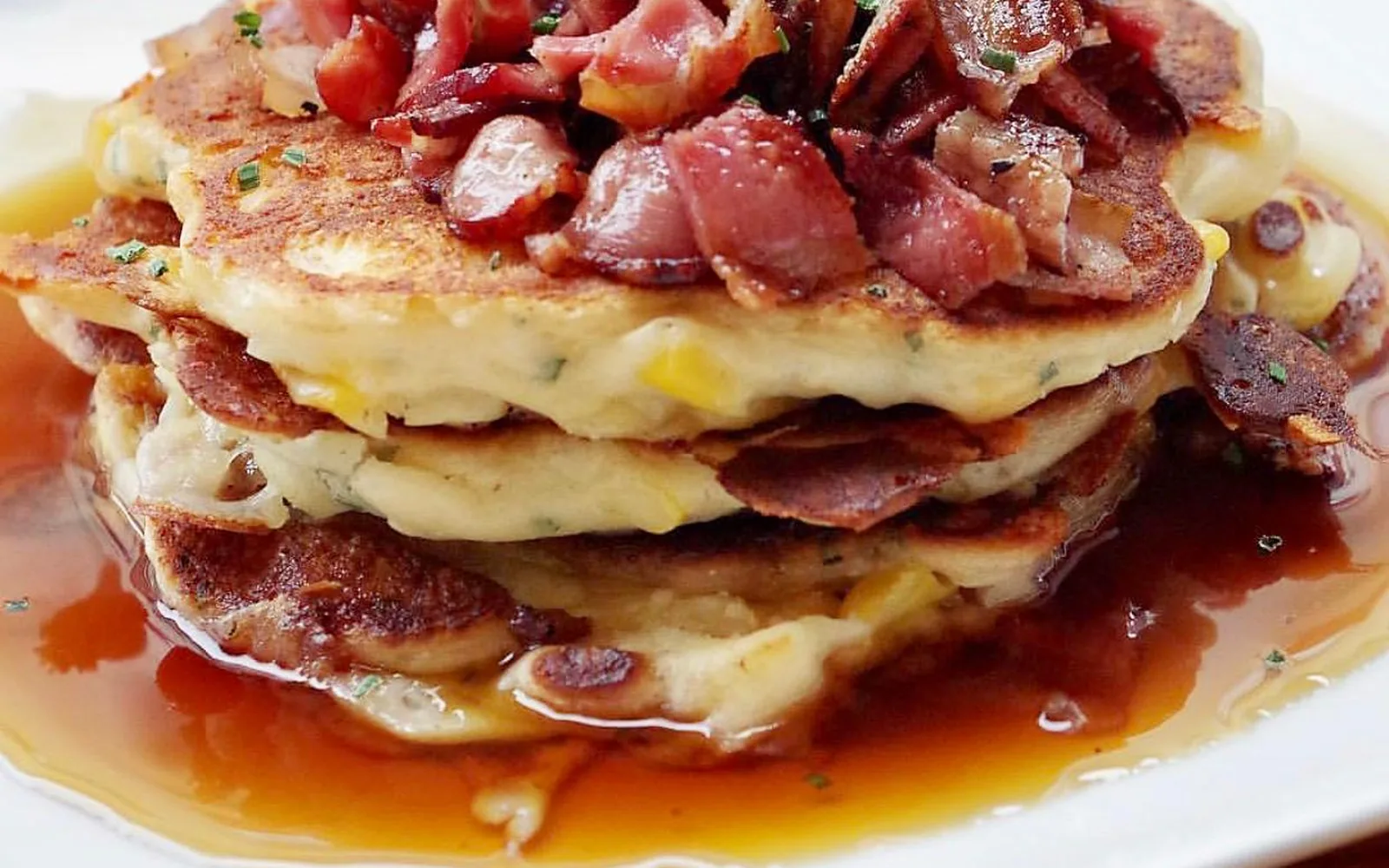 Cheddar, corn and chive pancakes stacked with crispy bacon and finished with maple syrup