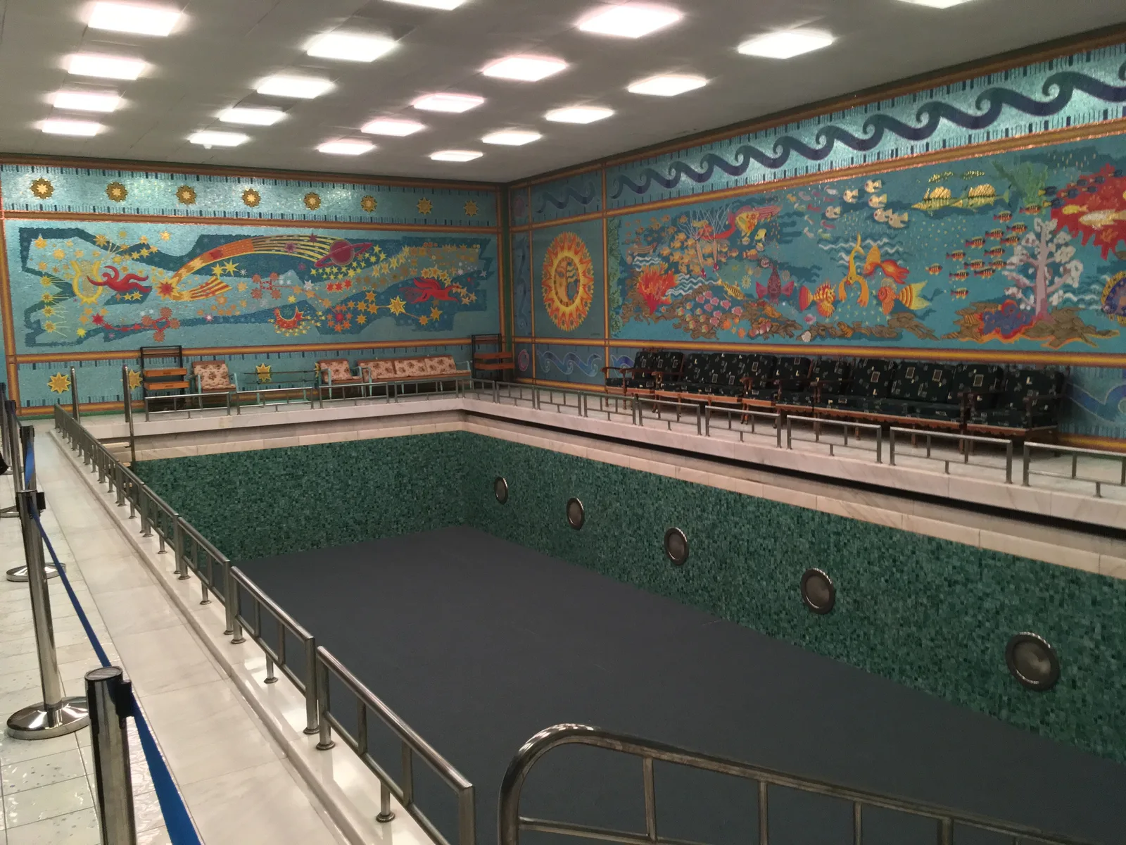The indoor swimming pool of the Primăverii Palace in Bucharest, lined with green tiles and surrounded by walls covered in colourful mosaics