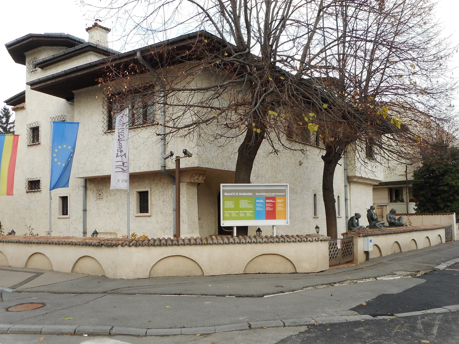 The Zambaccian Museum in Bucharest's Dorobanți district: a cream stucco villa behind a low tile-capped wall, with flags, a museum banner and a sign board out front