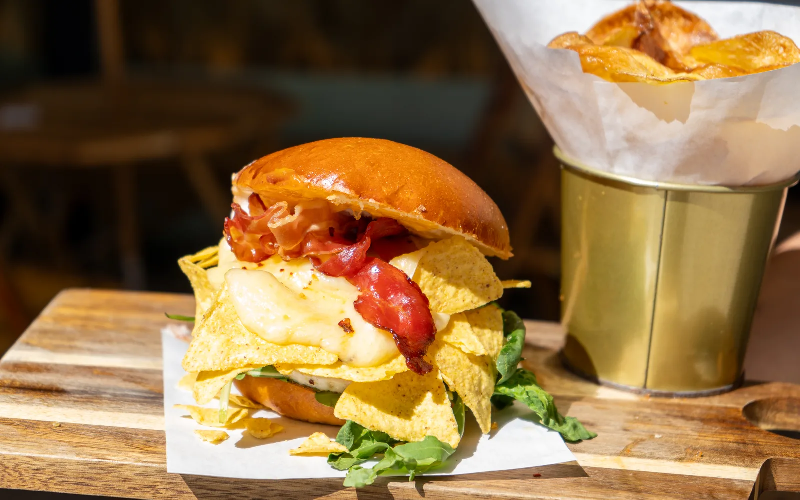 Breakfast Crunch Pretzelbun-Sandwich, the Ft 3,950 plate at Cookie Beacon Budapest: brioche bun, egg, bacon and tortilla chips on a wooden board with a tin of crisps on the terrace