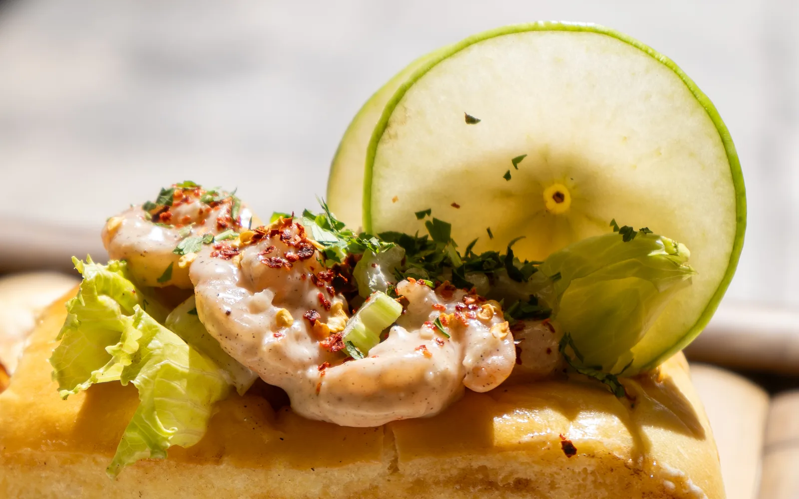 Close-up of the Cape Cod Shrimp Roll at Cookie Beacon Budapest: shrimp coated in aioli with diced celery and chili flakes on top of the toasted brioche, a pale green garnish standing behind