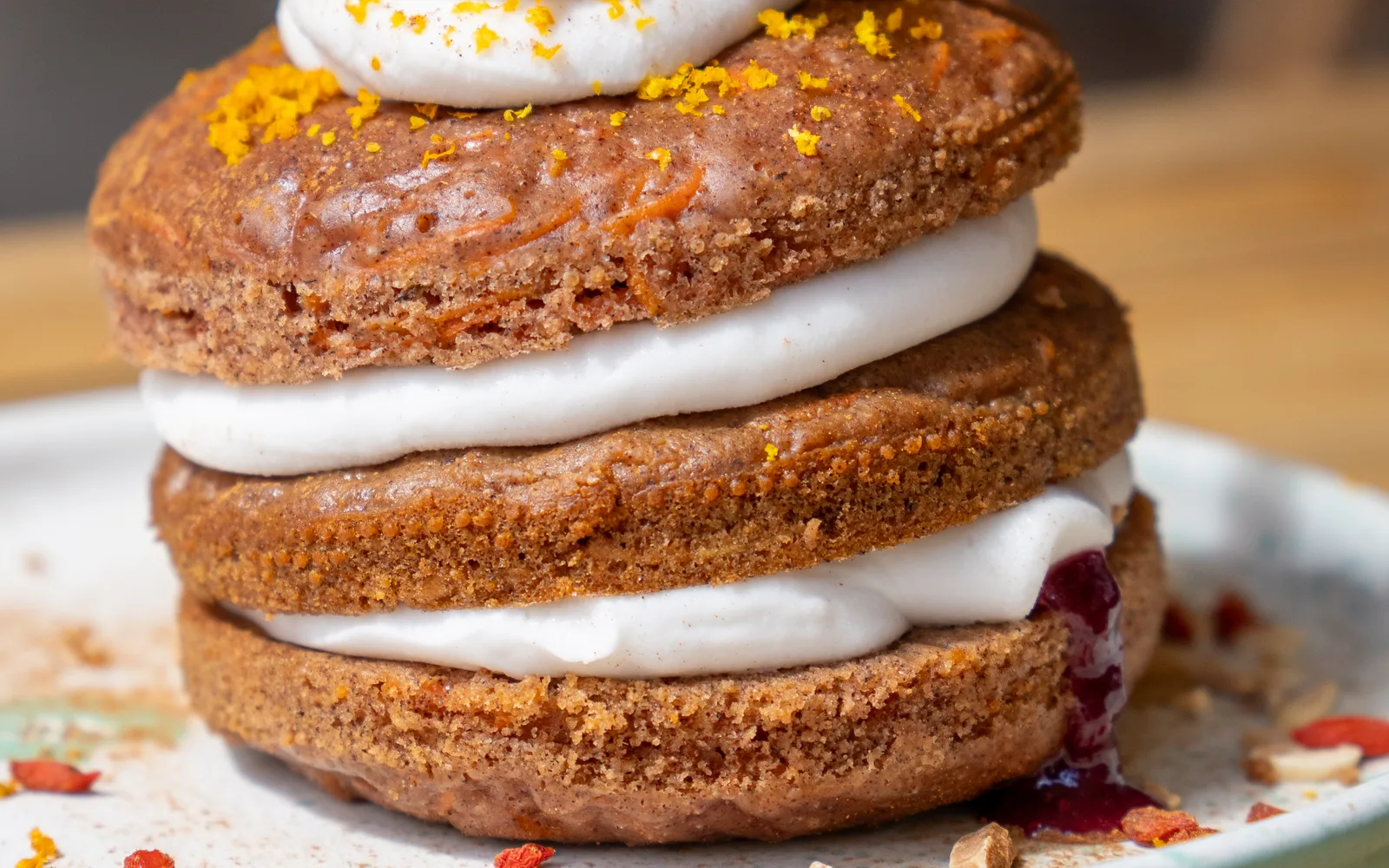 Close-up of the Carrot-Cake Pancakes at Cookie Beacon Budapest: strands of grated carrot in the pancakes, white cream between the layers, orange zest on top and dark berry jam running out of the bottom layer onto the plate