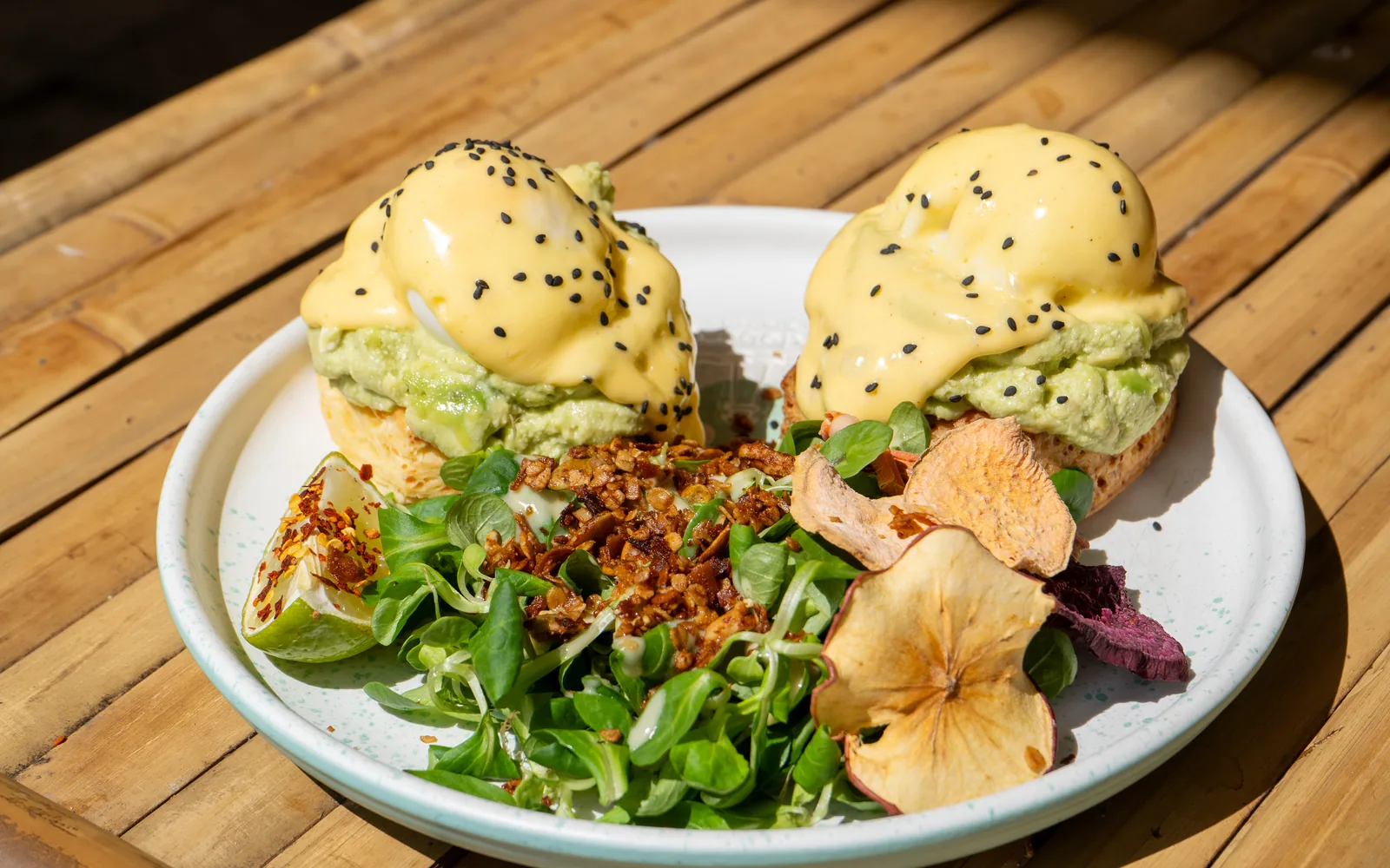 Eggs Benedict pe biscuiți cu cheddar la Cookie Beacon — ouă poșate sub sos olandez, pe biscuiți cu brânză, cu cremă de avocado și salată
