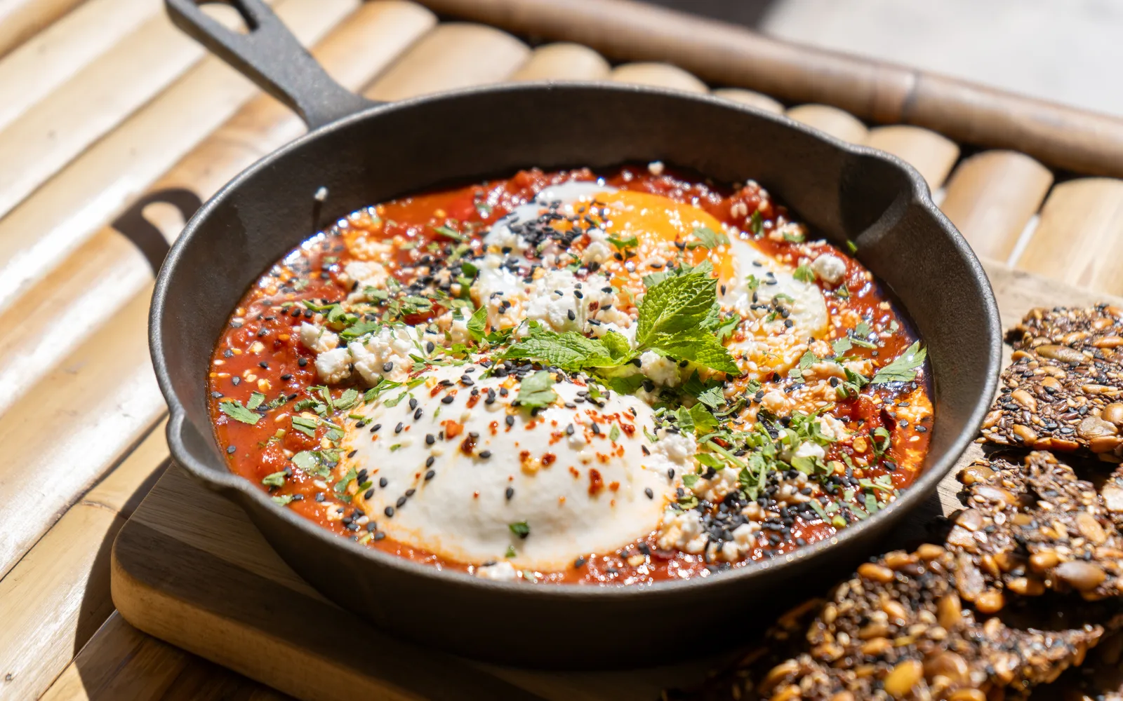 Close-up of the Shakshuka Burrata at Cookie Beacon Budapest: a white dome of burrata dusted with chili flakes and sesame in red tomato and pepper sauce, a sunny side up egg behind it, feta crumble and chopped herbs scattered over the cast-iron skillet