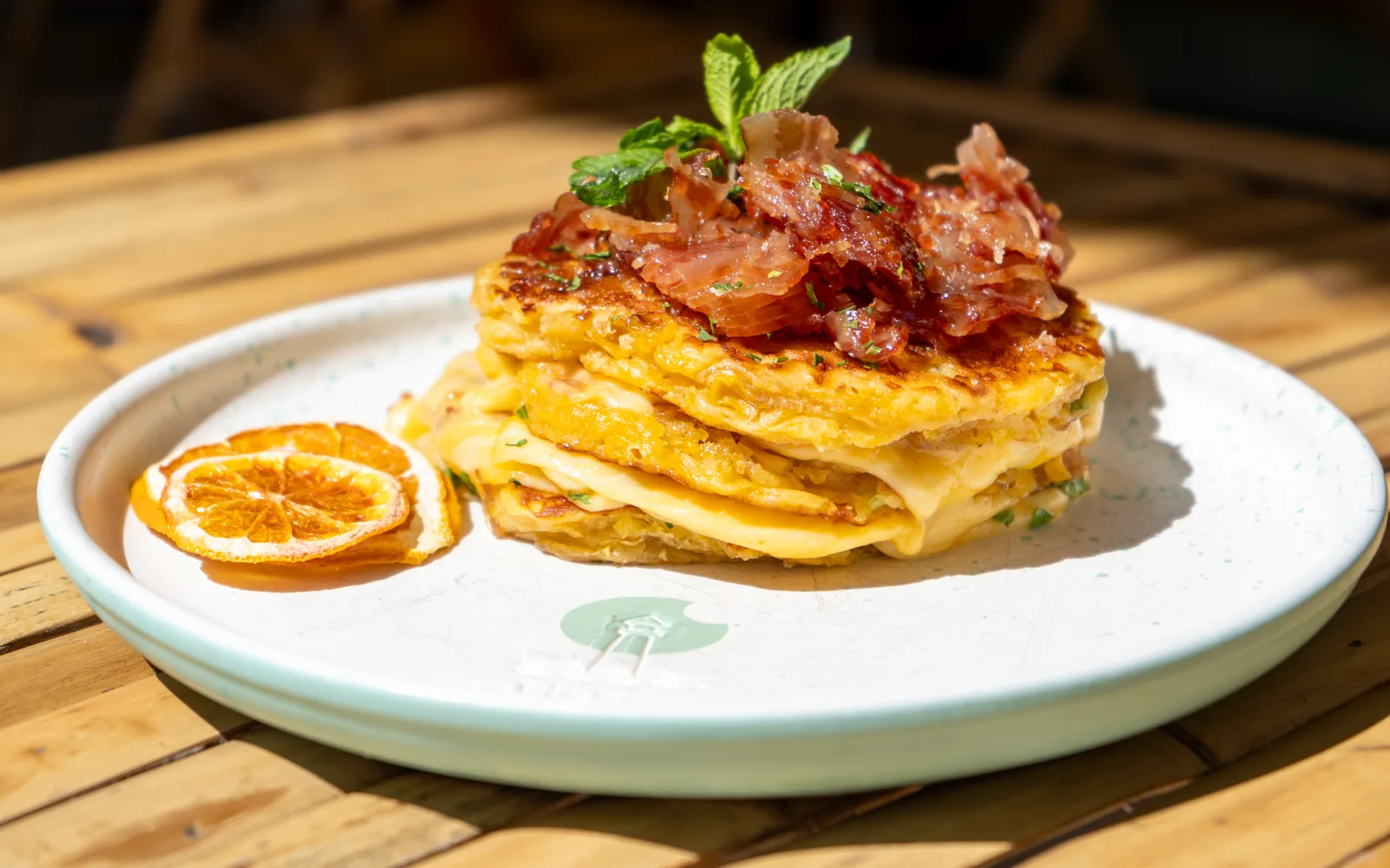Wild-West Breakfast Pancakes, a stack of sweet-corn pancakes with melted cheese and crispy bacon on a white plate, a dish on Cookie Beacon's Bucharest menu