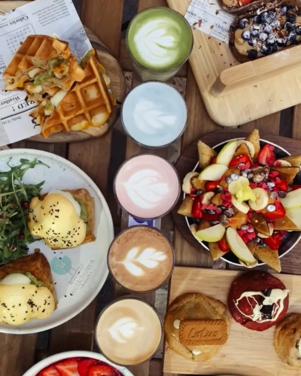 Brunch flat-lay with a waffle sandwich, granola bowls, lattes and cookies at Cookie Beacon