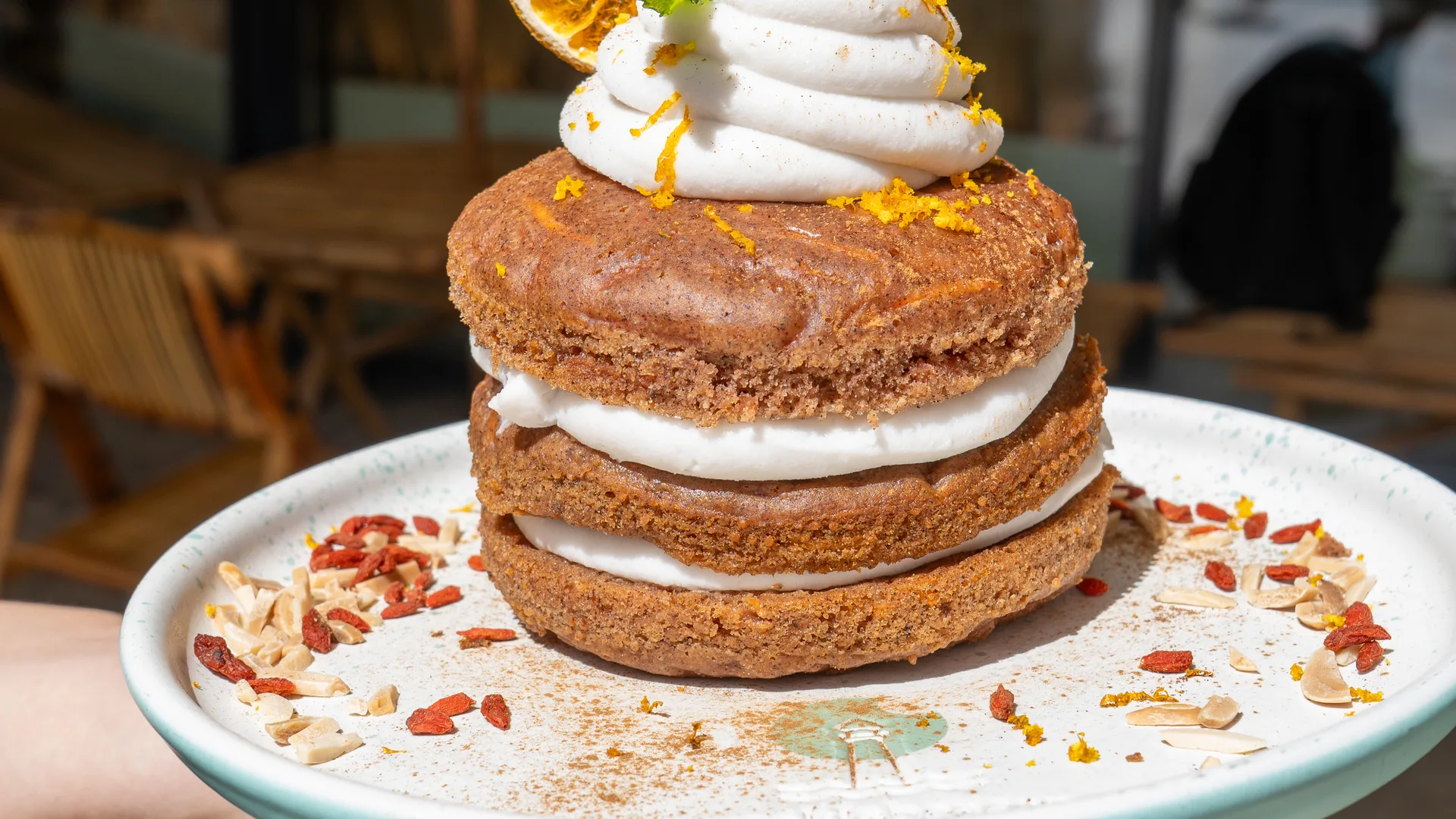 Carrot-cake pancake stack layered with cream, topped with dried orange, mint and an Oreo, with goji berries and almonds on the plate, at Cookie Beacon Budapest