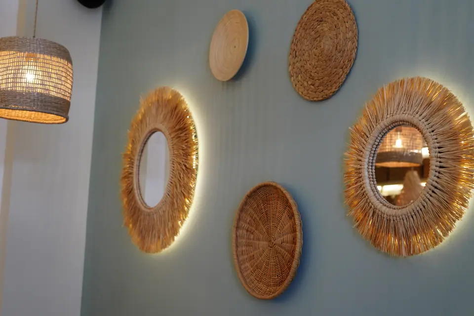 Round raffia-fringed mirrors and woven discs backlit on a sage-green wall at Cookie Beacon Kralja Petra in Belgrade, beside a rattan pendant lamp