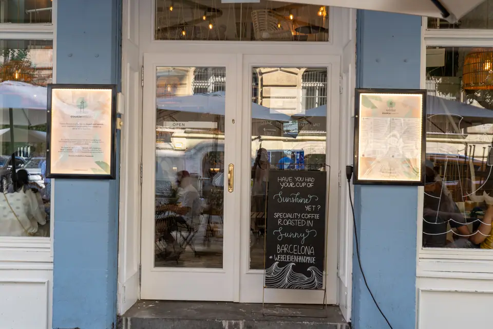 The white double doors of Cookie Beacon Budapest with a handwritten chalkboard listing specialty coffee