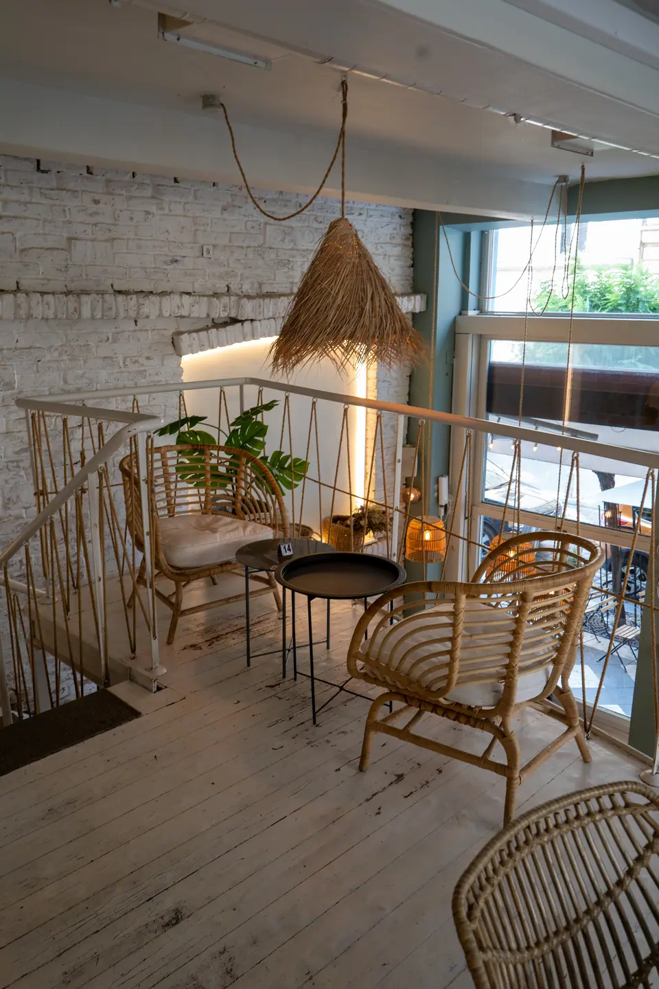 A corner nook at the top of the stairs at Cookie Beacon Budapest with a straw pendant lamp, rattan bench and plants