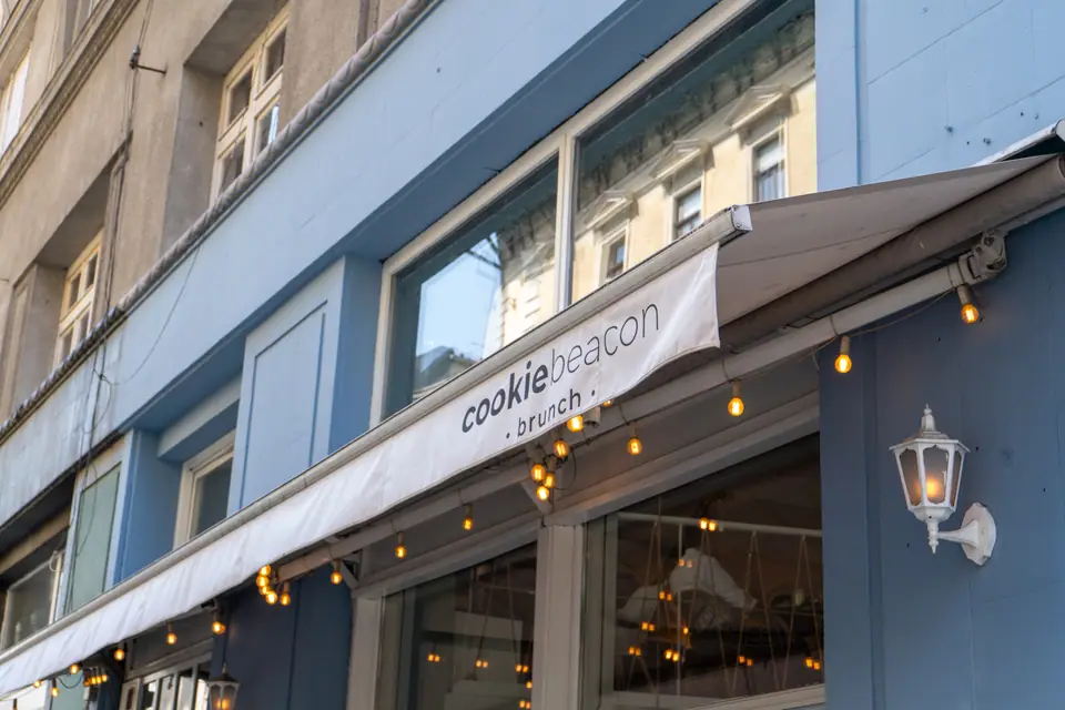 Festoon lights strung along the Cookie Beacon awning on the blue façade of the Lipótváros café at dusk
