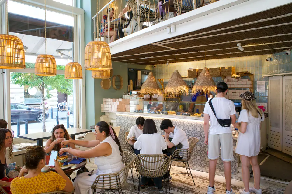 The ground-floor room at Cookie Beacon Budapest, rattan pendant lamps over tables and guests queueing at the counter