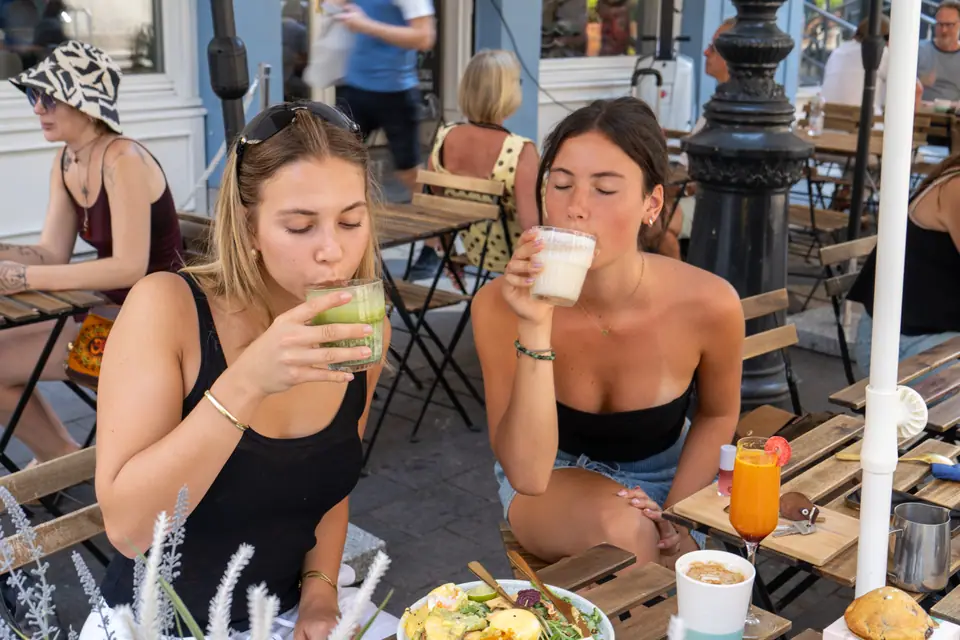 Two guests drinking a matcha and a coffee at a pavement table outside Cookie Beacon Budapest, brunch plates in front of them