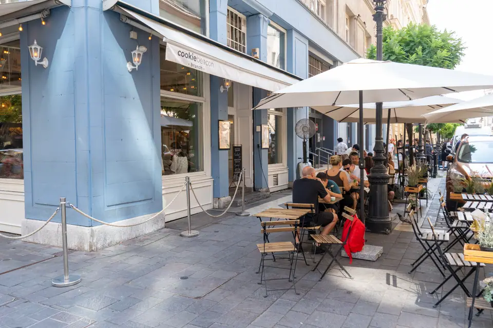 Guests sitting at pavement tables under parasols outside Cookie Beacon on a quiet Budapest street corner