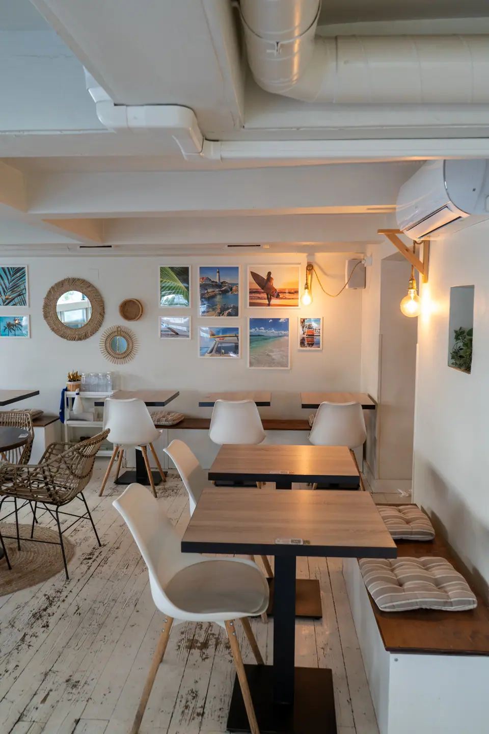 Empty tables and a bench under a wall of framed surf and coastal photographs in the upstairs room at Cookie Beacon Budapest