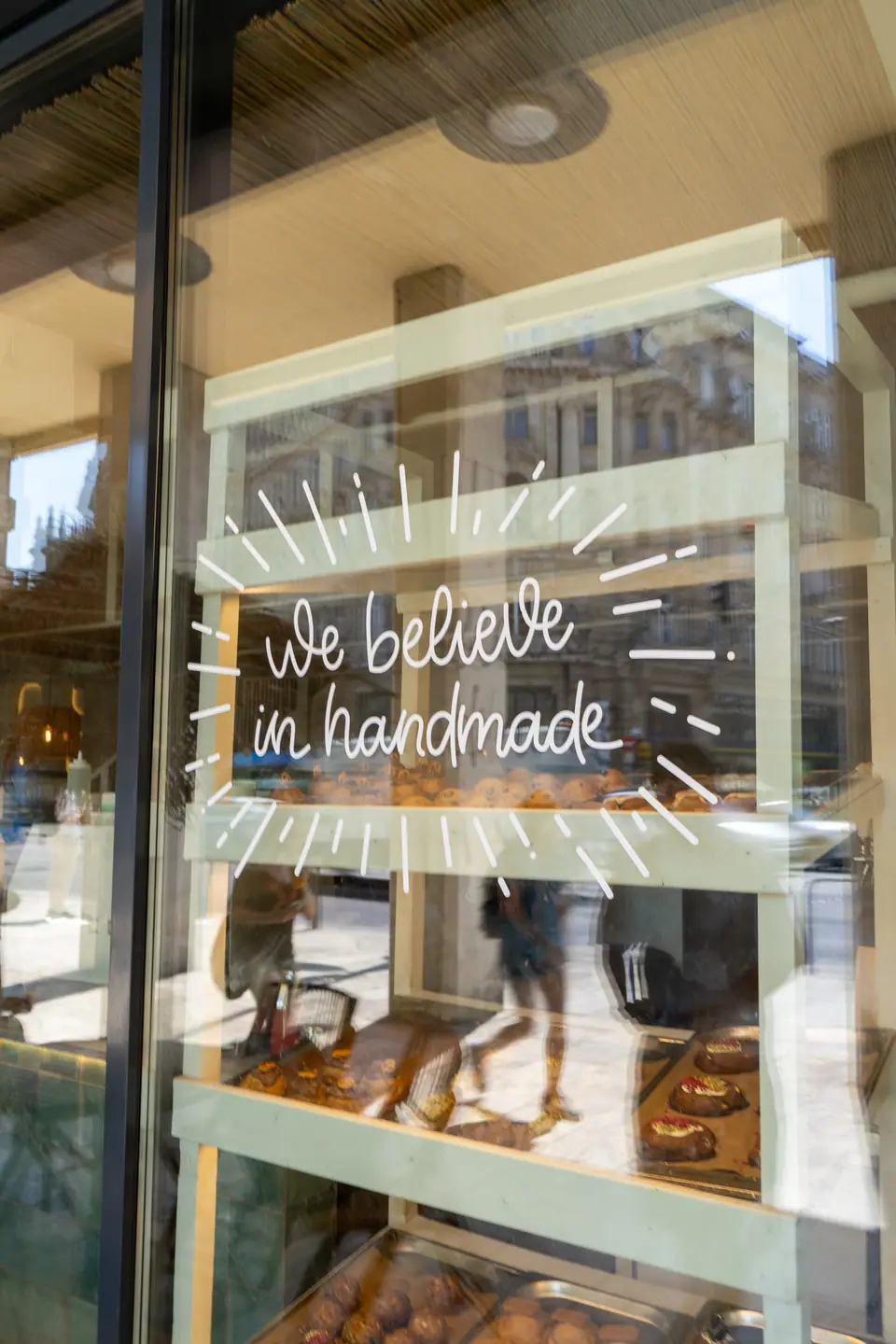 The hand-lettered window at Cookie Beacon Ferenciek tere with the pastry case behind the glass and the square reflected in it