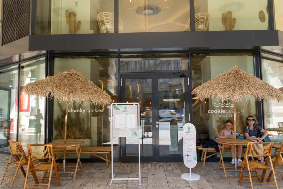 The Cookie Beacon storefront on Ferenciek tere in downtown Budapest, with straw parasols shading the pavement terrace