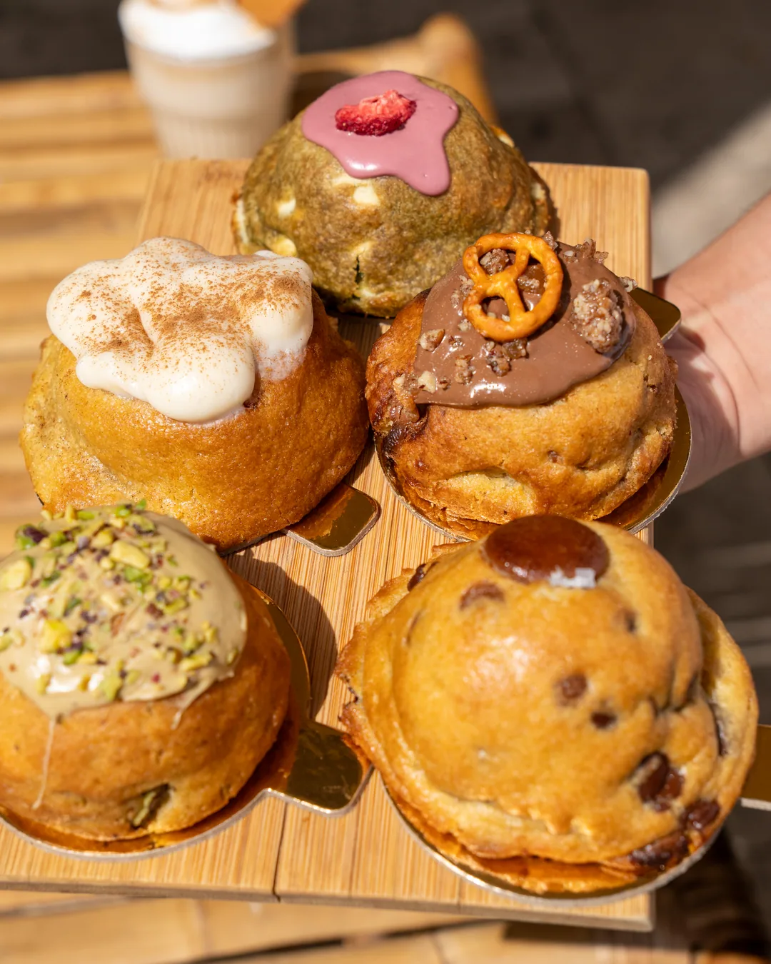 A hand holding a wooden board of Cookie Beacon chunky cookies, the chocolate chip one in front