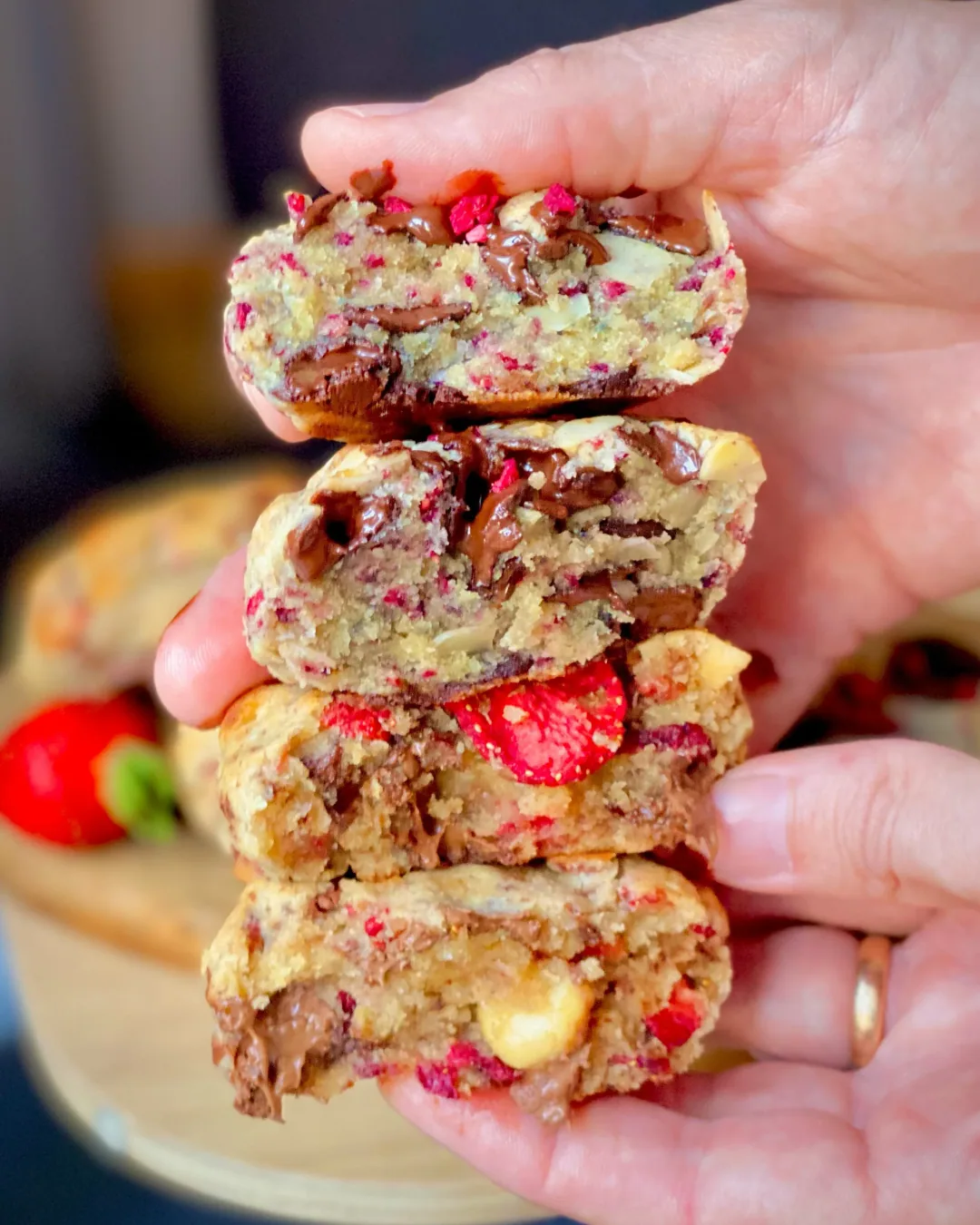 Hand holding a stack of split strawberry cookies showing melted chocolate and berry pieces